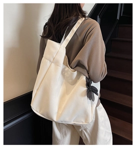 Minimalist beige canvas tote bag with a black bow accent shown on model at a staircase