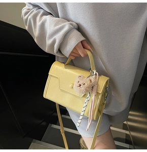 Detail of light yellow square handbag with leather texture and cute brown bear charm