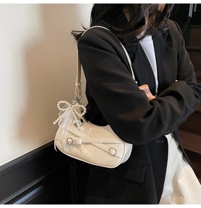 Detail of a creamy white half-moon shoulder bag featuring a pearl bow charm and metal buckle