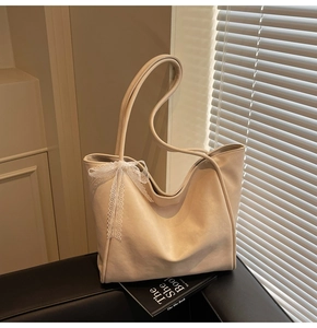 Detailed view of cream tote bag featuring a decorative lace bow on the shoulder strap