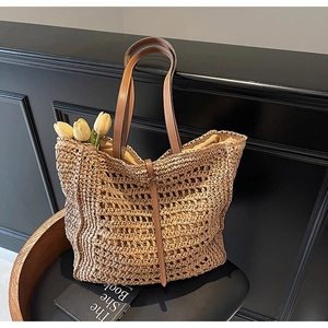 Detail of hollow-woven straw tote bag with brown leather handles and interior space