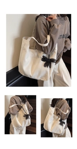 Detailed close-up of large cream canvas tote bag with black mesh bow charm accessory