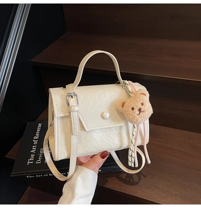 Detail of creamy white handbag with a pearl clasp and a cute brown plush bear charm