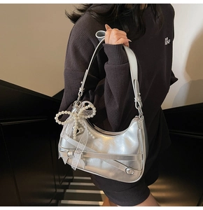 Detail of silver metallic underarm bag featuring a pearl bow charm and adjustable buckle