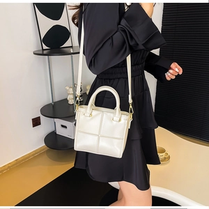 Détail du sac seau à carreaux blancs avec garniture dorée porté sur une robe noire
