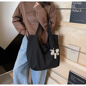 Close-up of black canvas tote bag with a white floral charm on a wooden shelf background