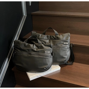 Detailed view of black nylon tote bags in two sizes on wooden stairs with branded labels