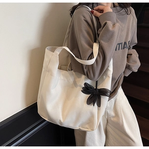Detail of white large-capacity canvas tote bag with black 3D bow charm accessory