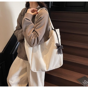 Detail view of white canvas tote bag with black bow pendant on a wooden staircase