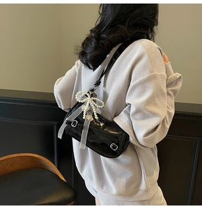 Detail of black patent leather underarm bag with pearl bow and silver buckle strap