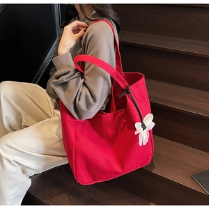 Detail of red canvas tote bag with white flower charm shown on model on wood stairs
