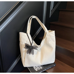 Detail of white canvas tote bag with black mesh bow charm on a stylish magazine
