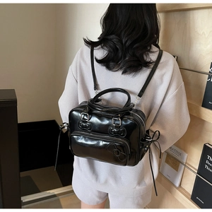 Detail of black patent leather backpack showing 3D bow elements and silver hardware