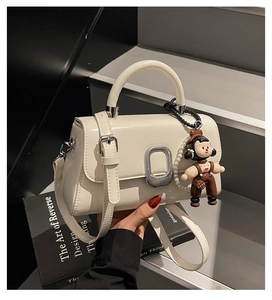 Detail of white leather handbag with silver oval buckle and a small trendy doll charm