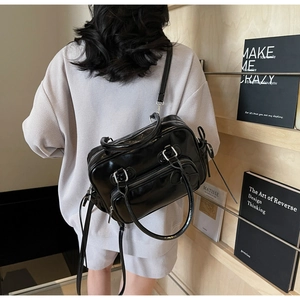 Detail of a black glossy multi-pocket crossbody bag worn by a model in a cozy library setting