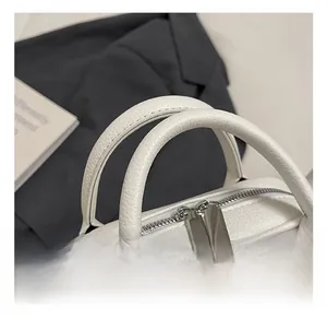 Detailed macro view of litchi grain white leather bag with dual zipper and round handles