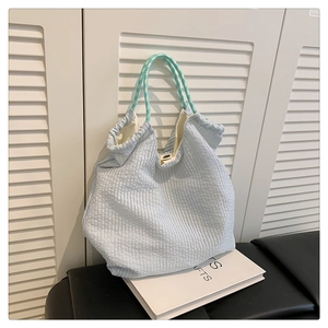 Détail du sac cabas en seersucker bleu clair avec anse en corde tressée sur un livre d'art