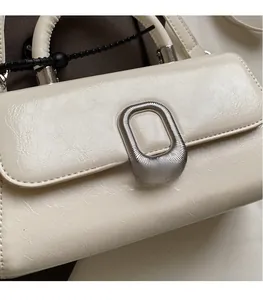 Detail of a creamy white handbag featuring a large silver oval metal buckle and leather texture