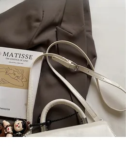 Elegant white square handbag with pearl pendant and adjustable strap on a stylish magazine