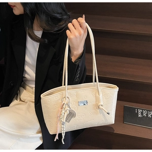 Chic cream tote bag with embossed bear pattern carried by model on wooden stairs
