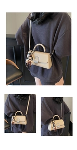 Detail view of beige crossbody bag with silver hardware and cartoon doll pendant