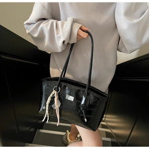 Close-up of black patent leather shoulder bag with embossed cartoon bear and woven charm