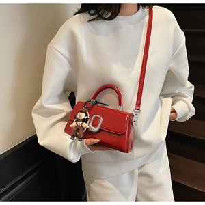 Detail view of a glossy red crossbody bag with silver buckle and a cute doll pendant