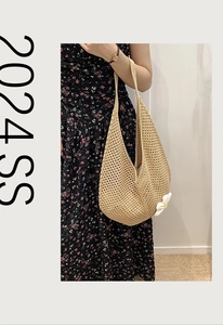 Detailed macro view of a large woven straw hobo bag with a white floral charm pendant