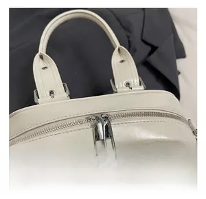 Detailed macro view of silver-polished double zippers and metal hardware on cream Boston bag