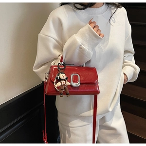 Glossy red handbag with silver buckle and cute doll charm worn over a white outfit