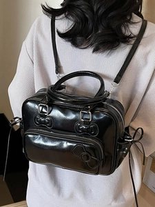 Glossy black bow-knot Boston bag with convertible straps shown on model in a grey sweater