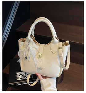 Detail of lychee textured leather bucket bag with pearl lace bow and gold metal clasp