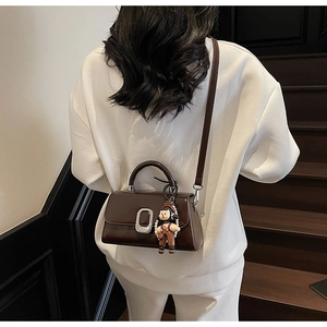 Close-up of a dark brown leather crossbody bag featuring a silver buckle and pearl chain