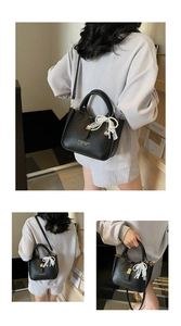 Macro detail of black lychee leather bucket bag with gold hardware and lace pearl bow