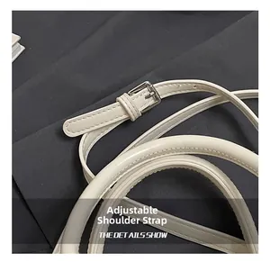 Detail view of the adjustable leather shoulder strap with silver metal buckle on cream bag