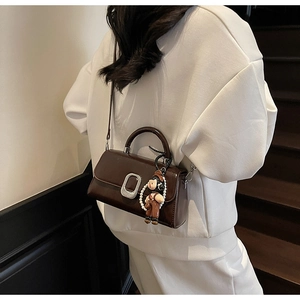 Detailed close-up of brown PU leather handbag with silver buckle and pearl doll charm