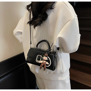 Detail of black glossy handbag with silver buckle and decorative pearl chain accent