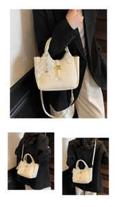 Detail view of cream lychee texture handbag featuring a lace bow and gold heart charm
