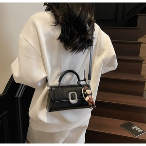 Close-up of black glossy leather handbag with silver square lock and cute doll pendant