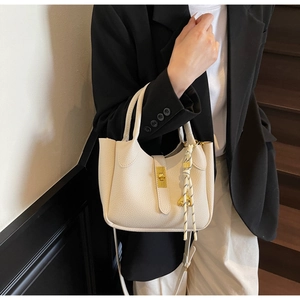 Dettaglio borsa a secchiello beige a grana con chiusura dorata e pendente sulla modella