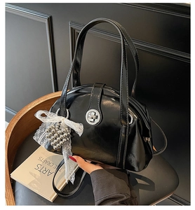 Détail du sac à main noir mat avec fermoir argenté et breloque en dentelle sur chaise en bois