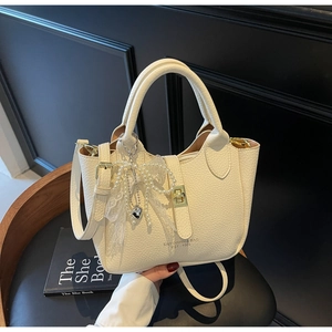 Close-up of beige lychee grain leather bucket bag with elegant pearl and lace heart charms
