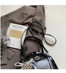 Détail du sac coquillage noir brillant avec boucle argentée et breloque en dentelle