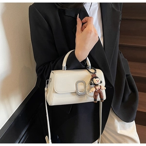 Detail of cream leather handbag featuring silver oval clasp and cartoon girl charm