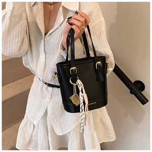 Close-up of black matte bucket bag featuring gold fashion logo and tennis racket charm