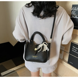 Detail of black lychee leather bucket bag with gold lettering and pearl bow charm