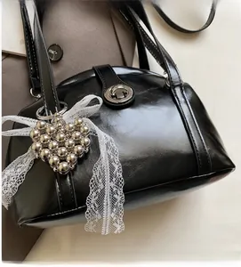 Détail d'un sac à main noir brillant avec serrure argentée et pendentif cœur en perles