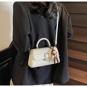 Detail of a creamy white rectangular leather handbag with silver oval buckle and cute charm