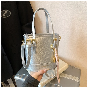 Detail of silver textured bucket bag with metallic finish and pink woven pendant charm