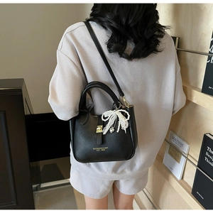 Detail view of black lychee grain bucket bag with pearl bow charm and gold magnetic clasp